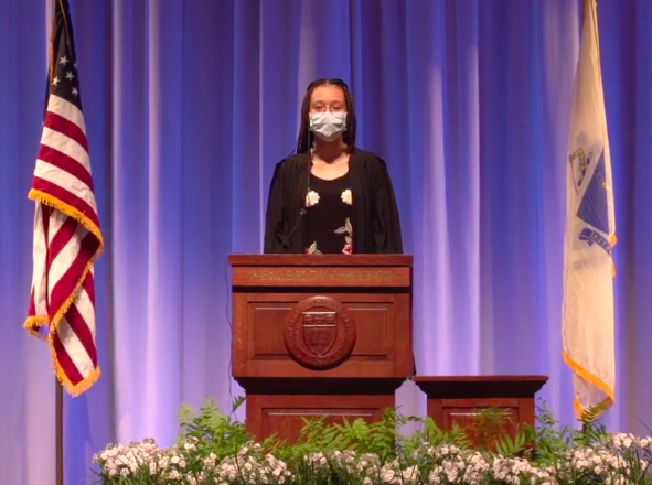 College Government President Tatiana Ivy Moise '21 speaks at commencement. She wears a mask and a graduation robe, and stands at a podium.