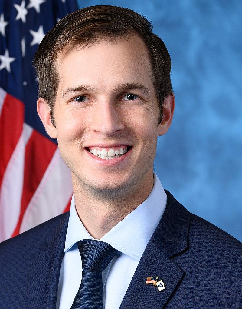 Image of Jake Auchincloss in front of a blue background and American Flag