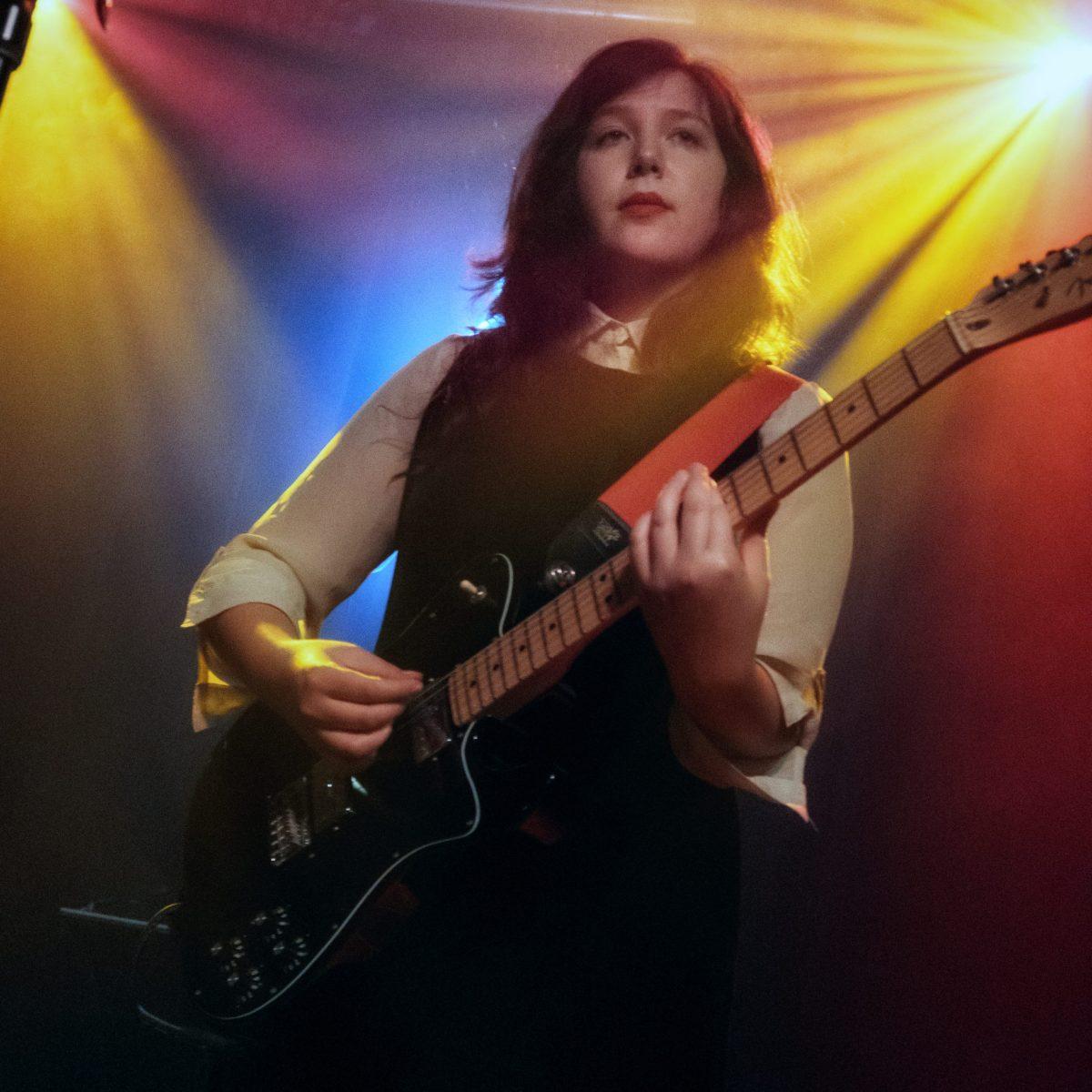 image of lucy dacus playing the guitar in multicolored lights.