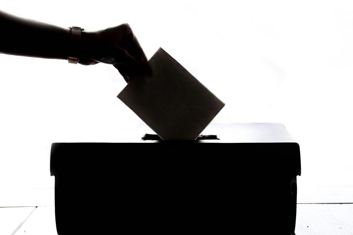 Backlit image of a hand placing a ballot in a box